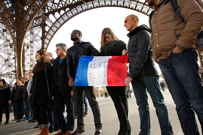 Paris residents take part in a moment of silence under the Eiffel Tower on Monday, Nov.16, in observance of those who died during the terrorist attacks three days ago. Holding a French flag with the words Liberty, Equality, Brotherhood, participants stand united during a minute of silence. 