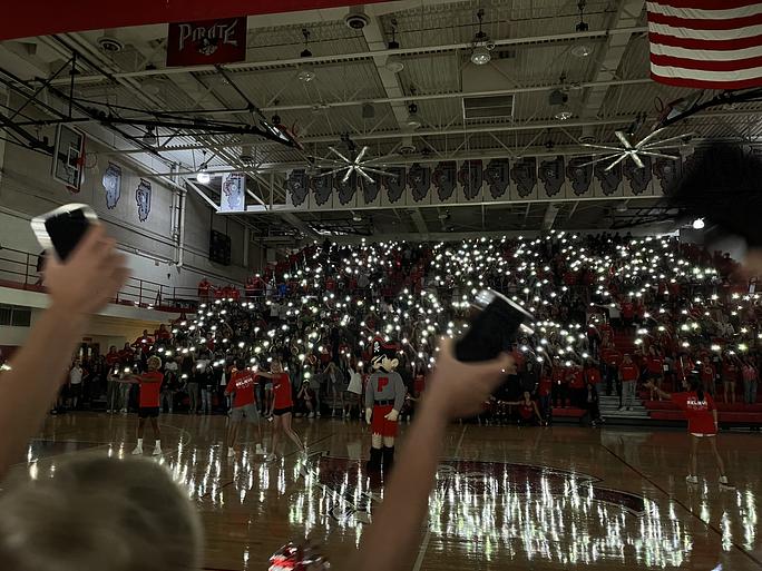 Students at Palatine High School join in synchronized movements of their phone flashlights in the darkness of the gym (Hala Habahbeh 2022). 