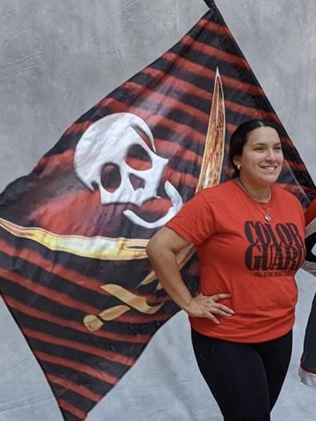 Varsity color guard coach Marisela Gonzalez poses for a picture behind a flag wielded by a color guard member.