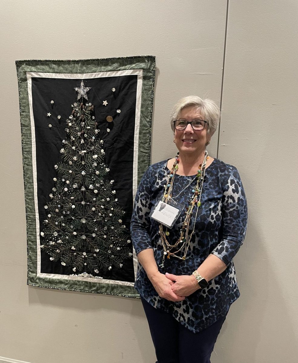 Button collector and designer Suzanne Proulx stands next to a tapestry with buttons she designed and created.