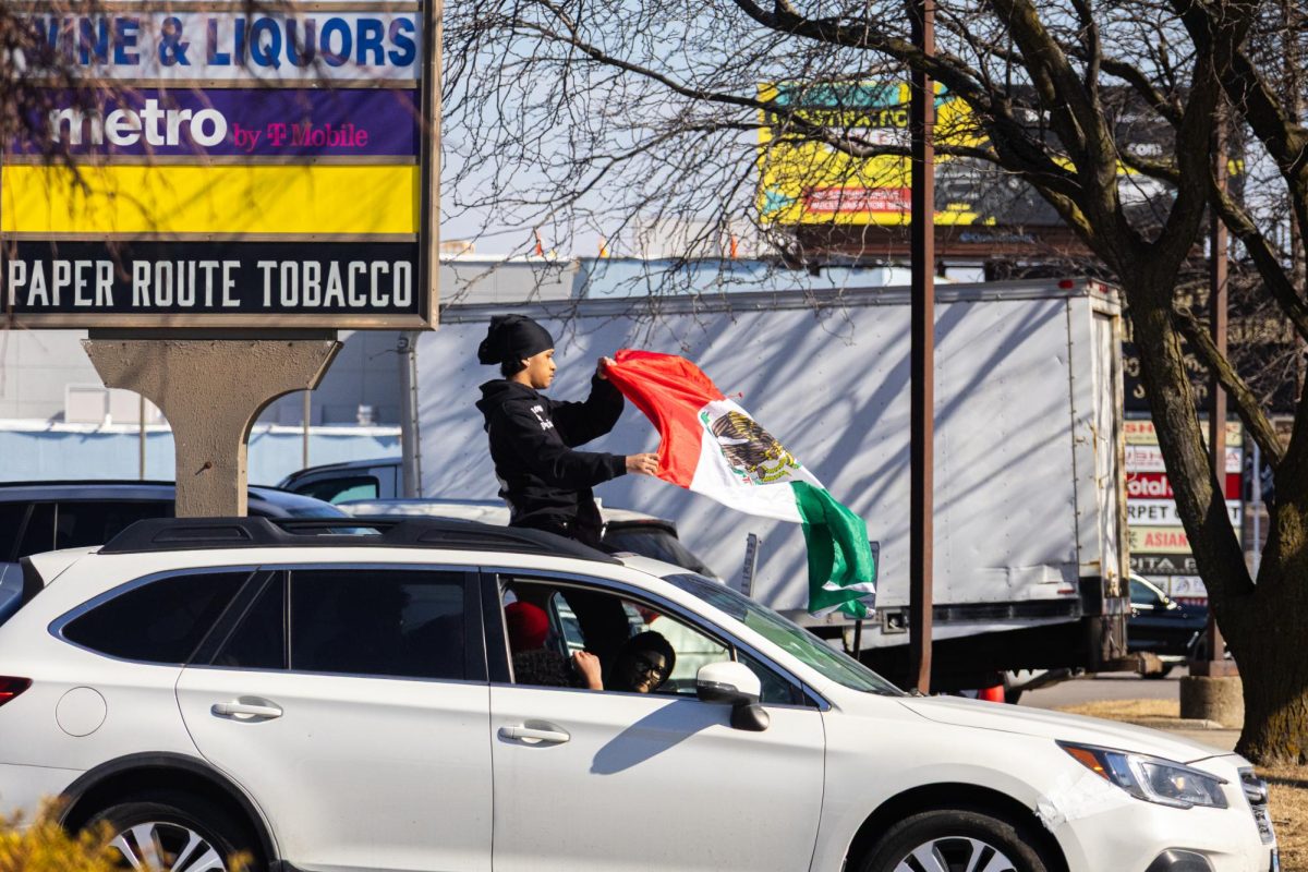 Students ride in a car alongside the march as a teenager stands through the sunroof waving a Mexican flag while joining the protest.